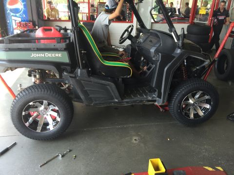 1988 Ford Bronco - A John Deere Gator UTV is shown in a service bay, custom wheels and a red gas can in the bed.