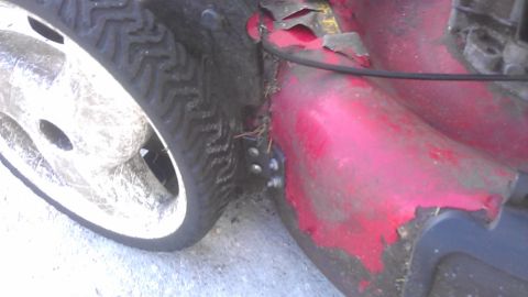 2006 Honda RANCHER - The red painted deck of a lawnmower shows wear and tear, with a close-up view of its wheel and tire.