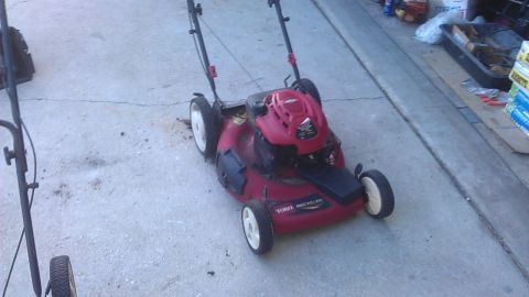 2006 Honda RANCHER - A red Toro Recycler lawn mower is parked on a concrete surface next to another lawn mower.
