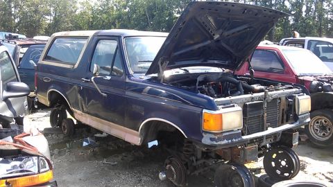 1994 Ford Bronco - Junkyard Ford Bronco, missing wheels and front bumper, hood is open showing the engine bay.