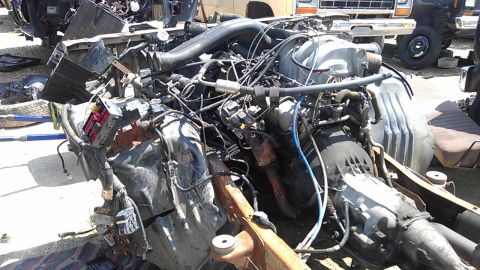 1994 Ford Bronco - A complex engine and transmission assembly sits in a junkyard, surrounded by other vehicle parts.