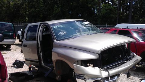 1994 Ford Bronco - A damaged silver pickup truck sits in a junkyard with its doors removed.