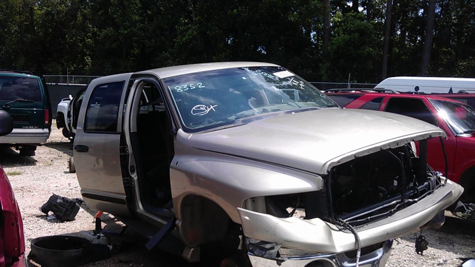 Silver pickup truck with front end damage and missing doors, parked in a junkyard