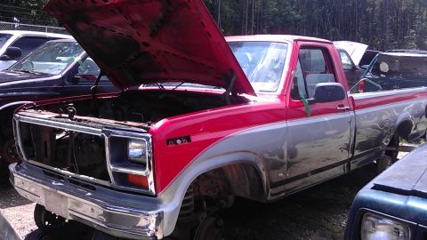 1994 Ford Bronco - This two-tone pickup truck, likely from the early 1980s, sits in a junkyard with its hood raised.