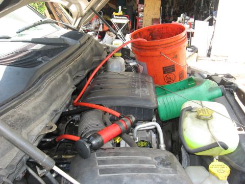1994 Ford Bronco - Fluid transfer pump in use within the engine bay, with an orange bucket and green jug nearby.