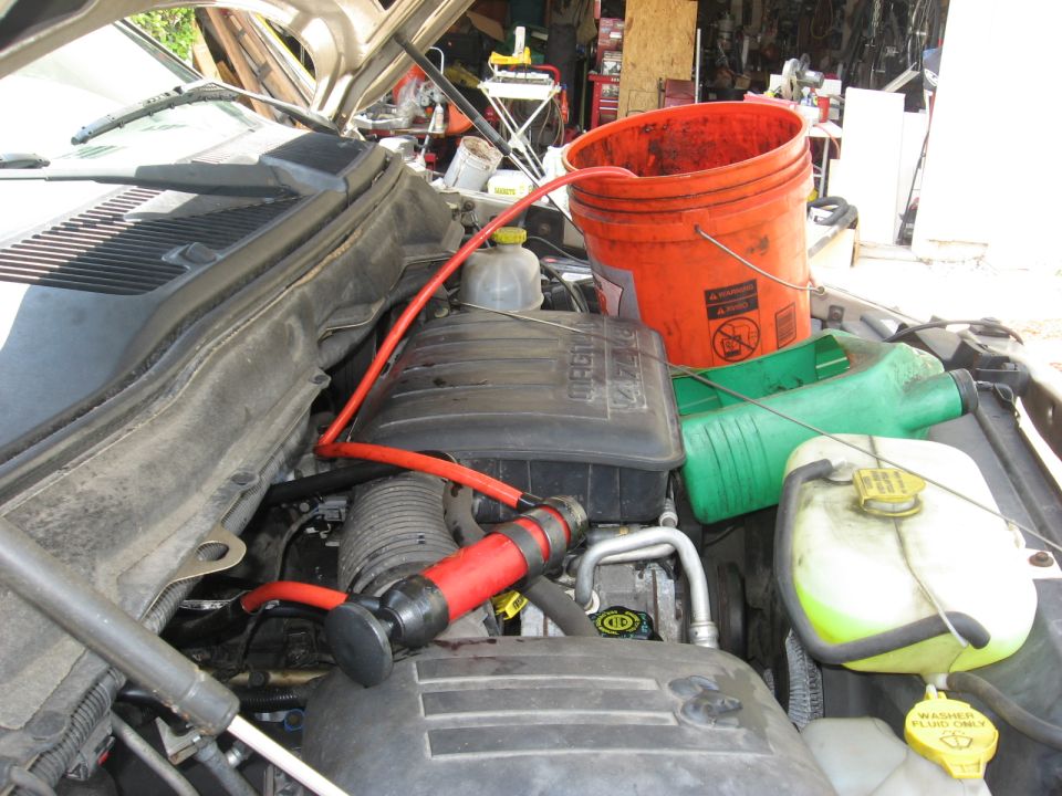 engine bay with red fluid transfer pump, orange bucket, and green jug