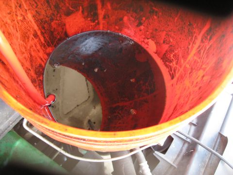 1994 Ford Bronco - Dark red transmission fluid fills an orange bucket, with a red hose visible.