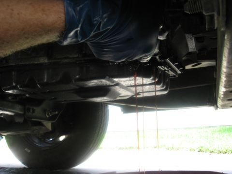 1994 Ford Bronco - Transmission fluid is draining from the pan. A gloved hand is visible working on the vehicle.