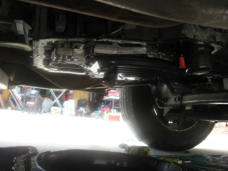 underside of vehicle, showing transmission pan and part of a tire. Drip pan visible below