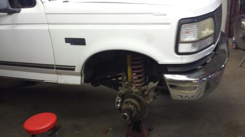 1996 Ford Bronco - The front wheel assembly of a white Ford truck is shown with the tire removed for maintenance.