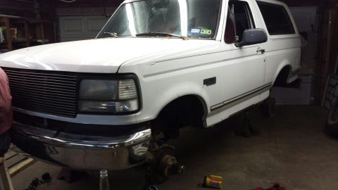 1996 Ford Bronco - 1996 Ford Bronco undergoing maintenance with front wheels off and vehicle elevated on jack stands.