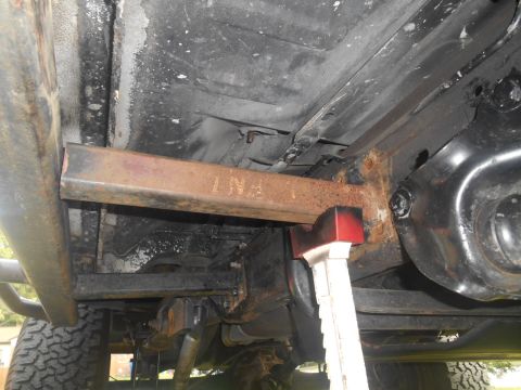 1994 Ford Bronco - The underside of a vehicle is shown, supported by a jack stand, with a rusty metal bar bearing the marking "LN7".
