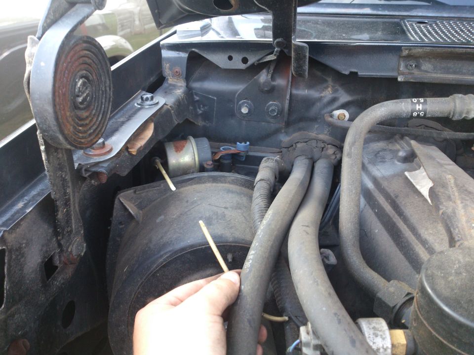 Close-up of engine bay with hoses and a hand holding a stick near a component