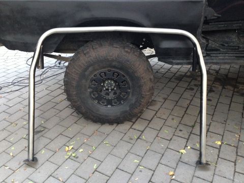 1979 Ford Bronco - A chrome roll bar is positioned in front of a large tire on a dark vehicle.