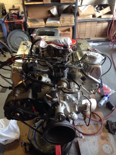 1978 Ford Bronco - Engine assembly with chrome valve covers and black belts on a stand in a garage.