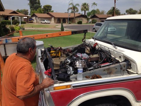 1978 Ford Bronco - A man is working on the engine bay of a truck, with the engine partially removed and an engine hoist positioned overhead.