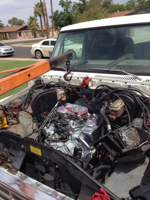 1978 Ford Bronco - Engine hoist is positioned to lift the engine out of the bay of a white vehicle.