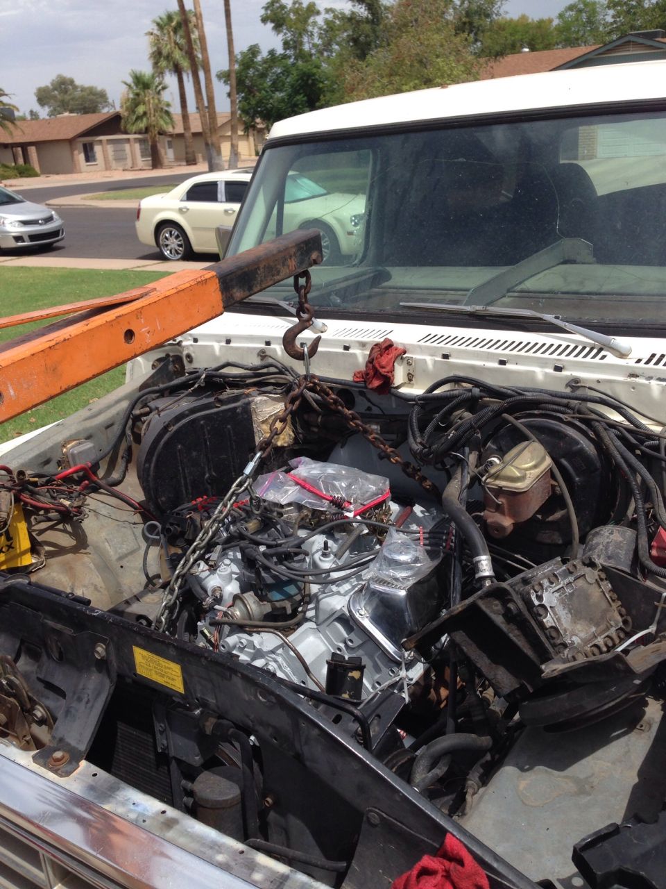 White vehicle engine bay with engine hoist lifting a chrome-accented engine