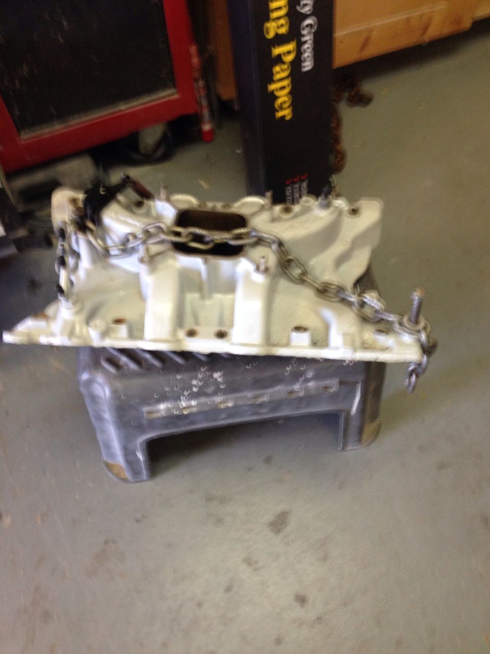 White engine intake manifold with a metal chain draped over it, resting on a gray stand