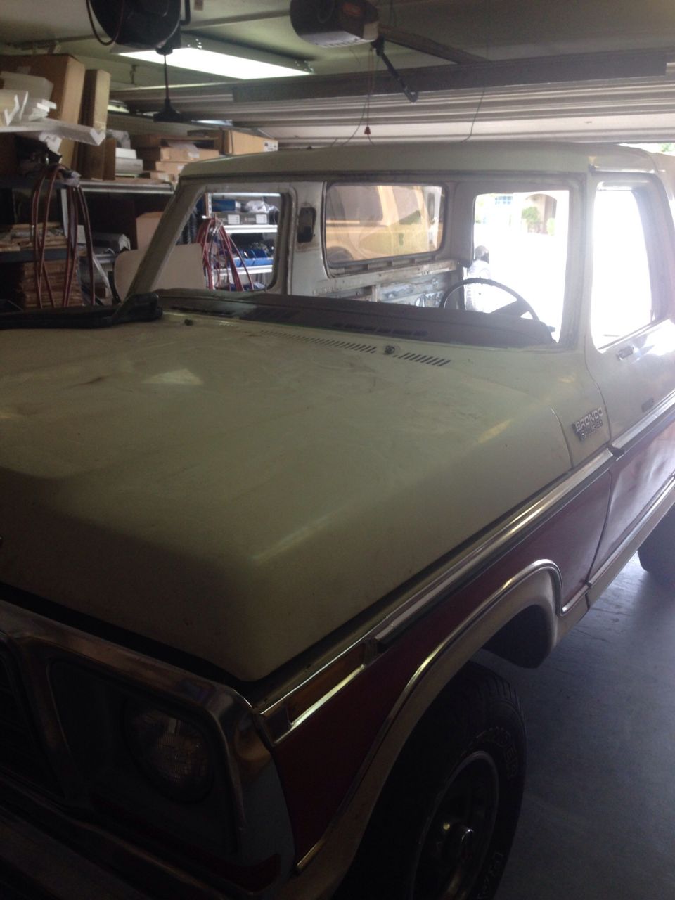 Dusty white and red 1978 Ford Bronco parked in a garage, front three-quarter view over the hood