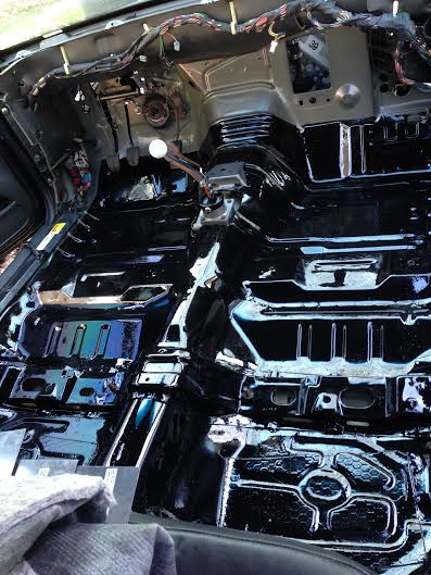 2004 Ford Crown Victoria - The interior floor pan of a car is coated in black, with exposed wiring and mechanical components visible.