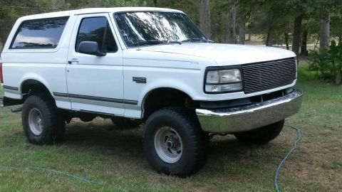 1996 Ford Bronco - A white Ford Bronco is parked on a grassy area with trees in the background.