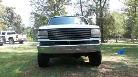 1996 Ford Bronco - White Ford F-Series truck with aftermarket grille and chrome bumper parked outside.