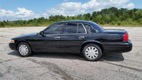 2001 Ford Crown Victoria - Side profile of a black 2001 Ford Crown Victoria sedan parked on a cracked asphalt lot.