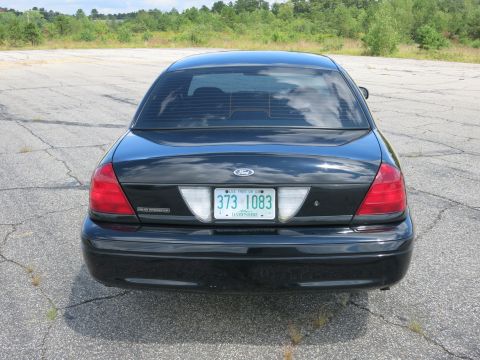 2001 Ford Crown Victoria - The rear of a black Ford Crown Victoria is parked on cracked asphalt with trees in the background.