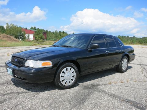 2001 Ford Crown Victoria - A black 2001 Ford Crown Victoria is parked on a cracked asphalt lot under a partly cloudy sky.