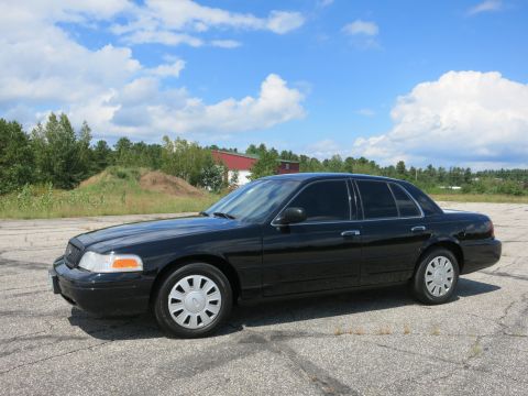 2001 Ford Crown Victoria - A black 2001 Ford Crown Victoria sedan is parked outdoors under a partly cloudy sky.