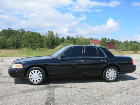 2001 Ford Crown Victoria - Side profile of a black 2001 Ford Crown Victoria sedan parked on cracked asphalt.
