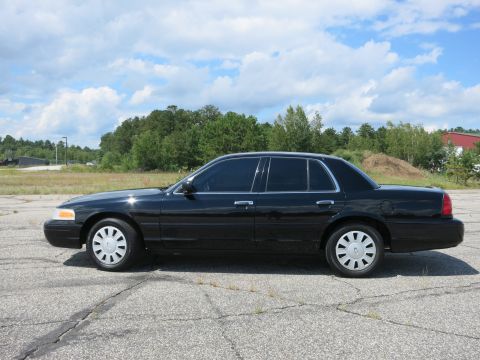 2001 Ford Crown Victoria - Side profile of a black 2001 Ford Crown Victoria sedan on a paved lot with trees in the background.