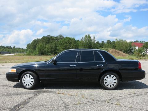 2001 Ford Crown Victoria - A black 2001 Ford Crown Victoria is shown from the side against a backdrop of trees and a cloudy sky.