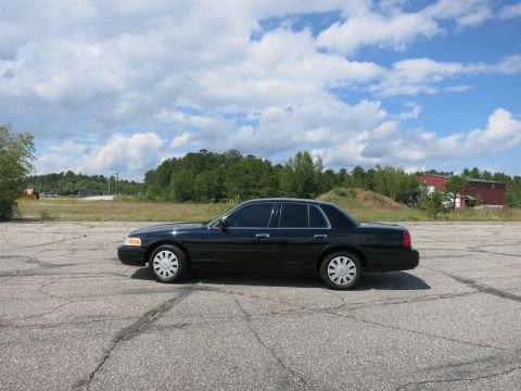 2001 Ford Crown Victoria - A black 2001 Ford Crown Victoria is seen from the side under a partly cloudy sky.