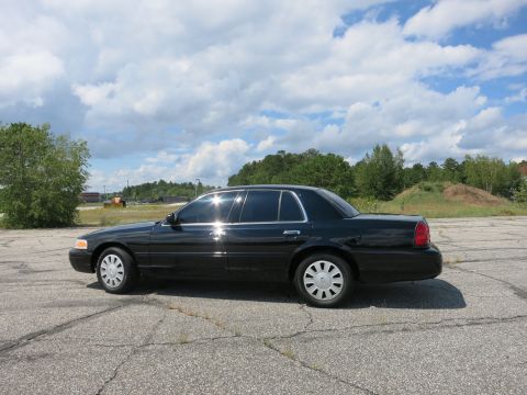 2001 Ford Crown Victoria - Side profile of a black 2001 Ford Crown Victoria sedan parked on cracked asphalt under a cloudy sky.