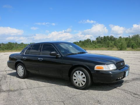 2001 Ford Crown Victoria - A black 2001 Ford Crown Victoria sedan is parked outdoors under a partly cloudy sky.