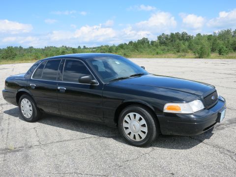 2001 Ford Crown Victoria - A black 2001 Ford Crown Victoria sedan is parked outdoors under a partly cloudy sky.