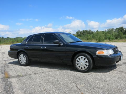 2001 Ford Crown Victoria - A black 2001 Ford Crown Victoria sedan is shown from a 3/4 front angle on a paved surface under a blue sky with clouds.