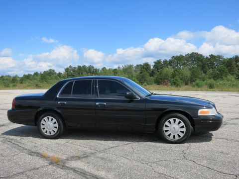 2001 Ford Crown Victoria - Side view of a black 2001 Ford Crown Victoria sedan under a partly cloudy sky.