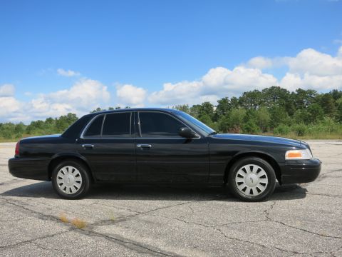 2001 Ford Crown Victoria - A black 2001 Ford Crown Victoria is seen from the side under a blue sky with scattered clouds.