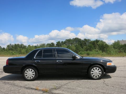 2001 Ford Crown Victoria - Side profile of a black 2001 Ford Crown Victoria sedan parked on asphalt under a partly cloudy sky.