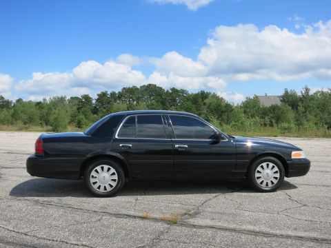 2001 Ford Crown Victoria - Side profile of a black 2001 Ford Crown Victoria sedan under a partly cloudy sky.
