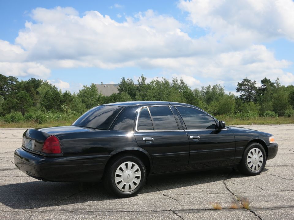 Black 2001 Ford Crown Victoria sedan, rear quarter view, parked on cracked asphalt