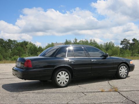 2001 Ford Crown Victoria - Side view of a black 2001 Ford Crown Victoria parked on cracked asphalt under a cloudy sky.