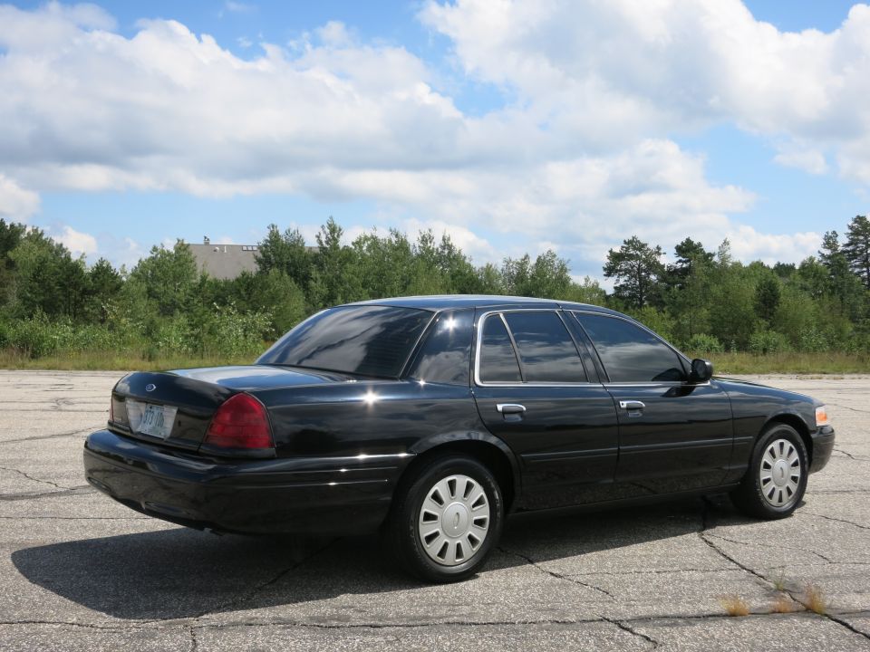 Black 2001 Ford Crown Victoria parked on asphalt with trees and sky in background