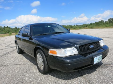 2001 Ford Crown Victoria - This black Ford Crown Victoria is shown from a three-quarter front view on a paved surface with trees in the background.