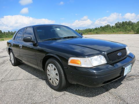 2001 Ford Crown Victoria - A black sedan with a distinctive grille and headlights is parked outdoors under a partly cloudy sky.