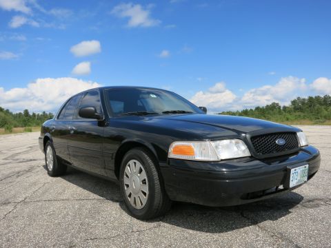 2001 Ford Crown Victoria - Black 2001 Ford Crown Victoria shown from a 3/4 front angle with a clear blue sky and scattered clouds in the background.