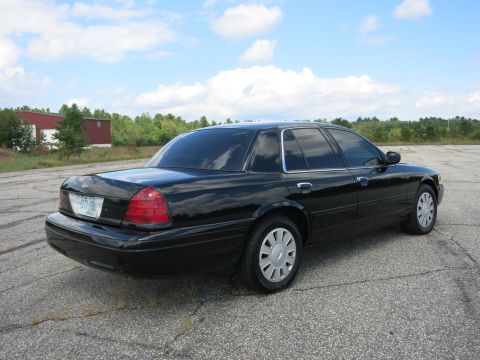 2001 Ford Crown Victoria - This black sedan is parked on an asphalt lot with a building and trees in the background under a cloudy sky.